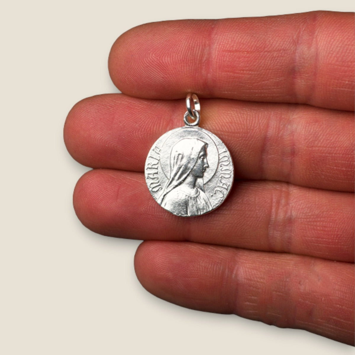 Medalla de la Virgen de Lourdes y María Inmaculada en plata - 20mm sobre una mano