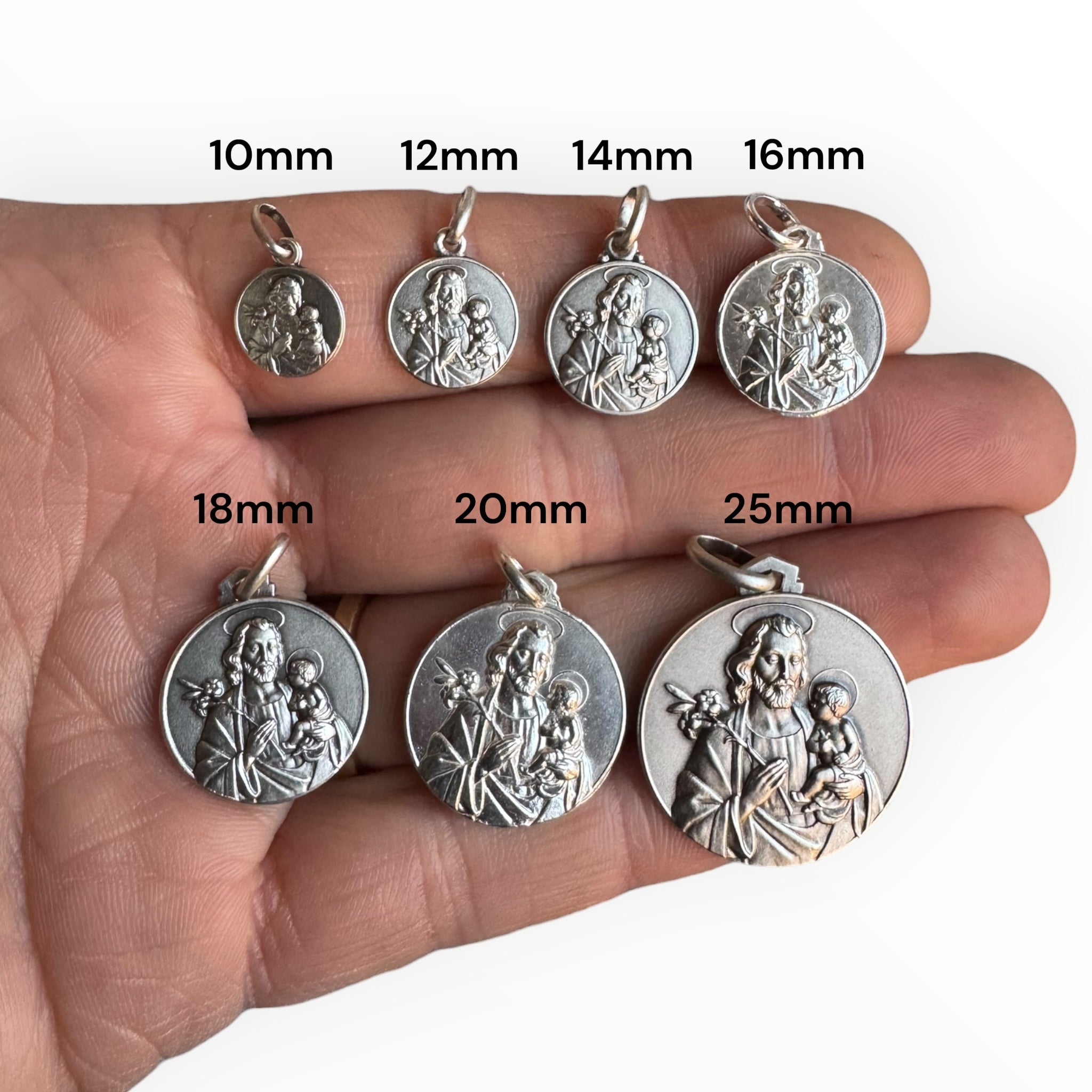 medallas de san josé de plata sobre una mano para comparación de tamaños